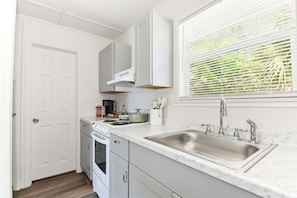 A kitchen with white cabinets, a stainless steel sink, a stove, and a window with blinds. - Riverfront Home with Guest House, Deck and Yard (Melbourne)