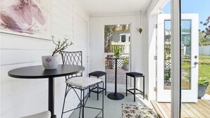 Un espace patio avec une table et deux chaises, une petite plante en pot et une vue sur l’extérieur.