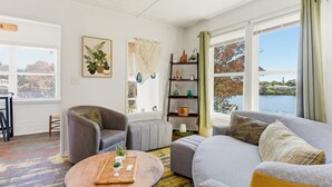 Un salon comprenant un canapé, un fauteuil et un pouf, une table basse en bois, une bibliothèque et une vue sur une étendue d’eau.