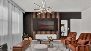 A modern living room with a sofa, ottoman, and armchairs, a coffee table, a TV, and a unique ceiling light fixture. - Luxury Themed Villa w/ Pool, Game Room, Resort (Davenport)