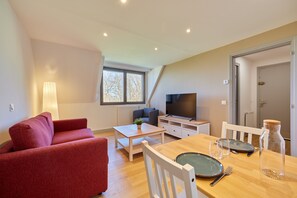 Un apartamento moderno con sofá rojo, mesa de comedor de madera, televisor y ventana con vistas.