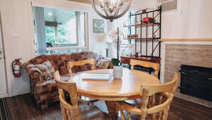 A cozy living area with a wooden dining table, cushioned seating, a fireplace, and a bookshelf. - Nature Escape and Miller Zoo | Buddy Shack (Frampton)