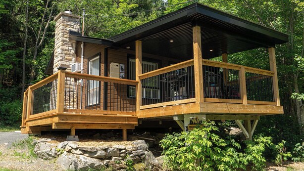 A wooden cabin with a stone chimney, a covered deck, and a sign indicating a 'BUDDY' establishment. - Nature Escape and Miller Zoo | Buddy Shack (Frampton)