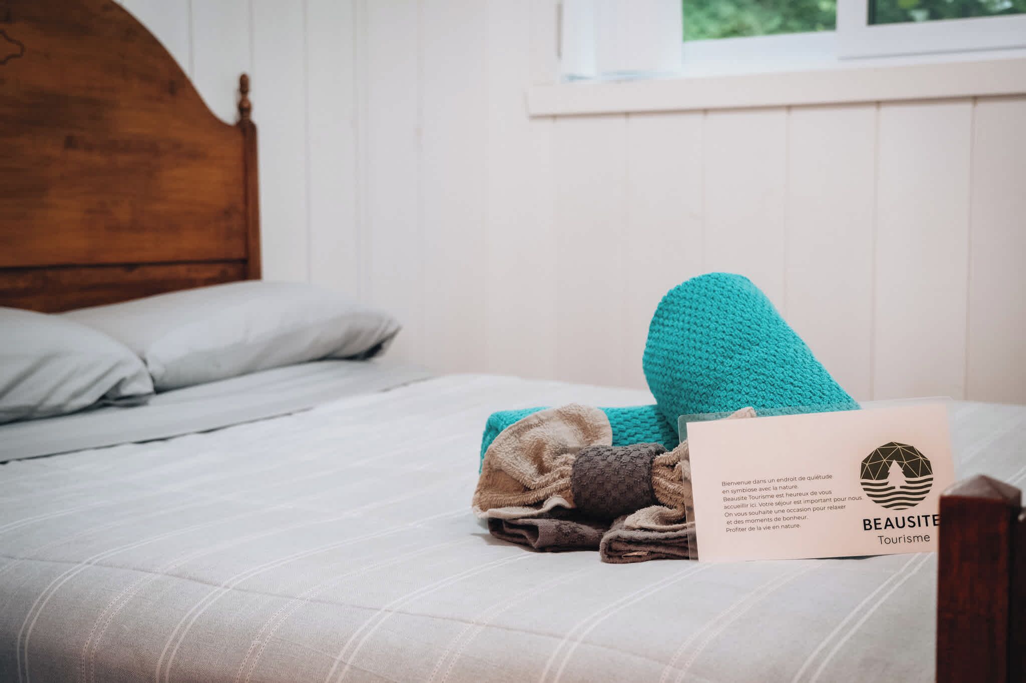 Un lit bien fait, avec une tête de lit en bois, une serviette pliée et une carte posée sur le lit.