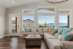 Ein geräumiges Wohnzimmer mit einer großzügigen Eckcouch, einem Couchtisch und mehreren Fenstern mit Blick auf Strand und Berge.