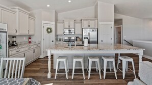 Een moderne keuken met witte kasten, een groot kookeiland met barstoelen en geïntegreerde apparatuur.