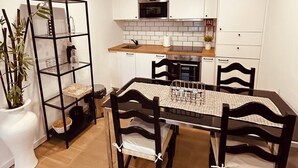 Una cocina moderna con armarios blancos, una estantería de metal negro y una mesa de comedor con sillas.