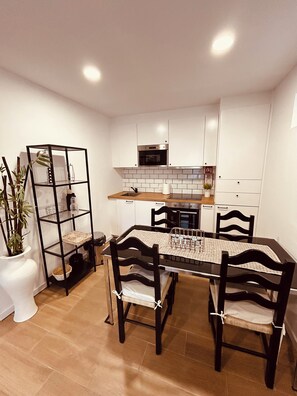 Une cuisine moderne avec des meubles blancs, une étagère en métal noir et une table à manger avec des chaises.