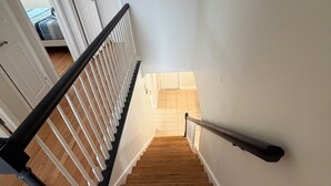 Eine Holztreppe mit weißen Wänden und einem schwarzen Geländer, die zu einem Zimmer mit einem Bett und einer Tür führt.