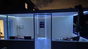Ein modernes Zimmer mit Glastrennwand, einem Laptop und einem Fernseher auf einem Standfuß.