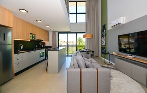 A modern kitchen with built-in appliances, a dining area with a sofa, and a large TV. - Moderno Loft na Lagoa da Conceição  (Florianópolis)