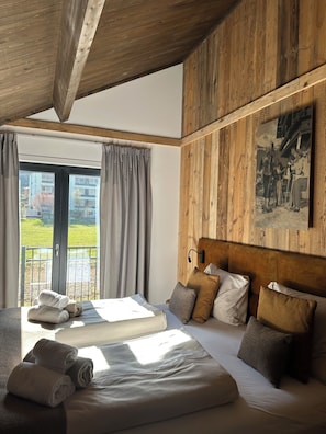 Ein Hotelzimmer mit einem großen Bett, einem Balkon mit Vorhängen und einer Holzwand mit einem Bild.