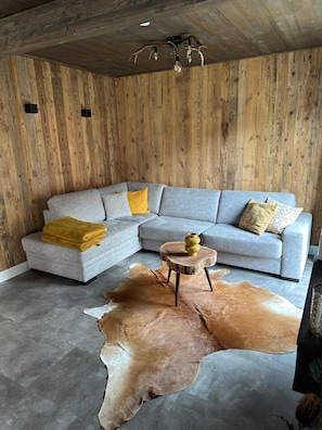Ein modernes Wohnzimmer mit einem grauen Ecksofa, einem Holztisch und einem großen Teppich aus Leder.