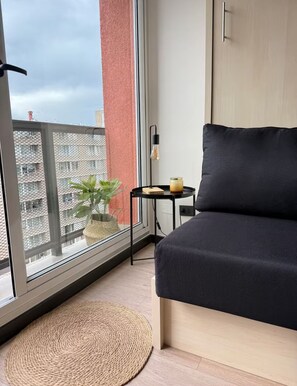 Et moderne soveværelse med et stort vindue, et lille bord med et lys og en potteplante.