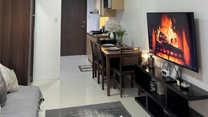 A modern living room with a flat-screen TV, a dining area with wooden furniture, and a kitchen with a microwave. - Cozy Studio Room with Fitness Gym (Baguio)