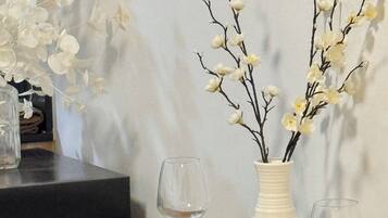A dining table set with plates, bowls, and wine glasses, accompanied by a vase with branches and flowers.