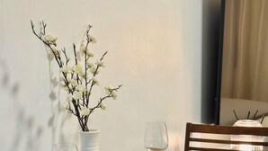 A dining table set with white plates, bowls, and wine glasses, accompanied by a white vase with branches. - Cozy Studio Room with Fitness Gym (Baguio)