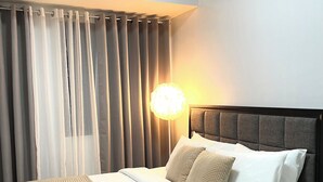 A modern bedroom with a bed, a bedside lamp, and sheer curtains. - Cozy Studio Room with Fitness Gym (Baguio)