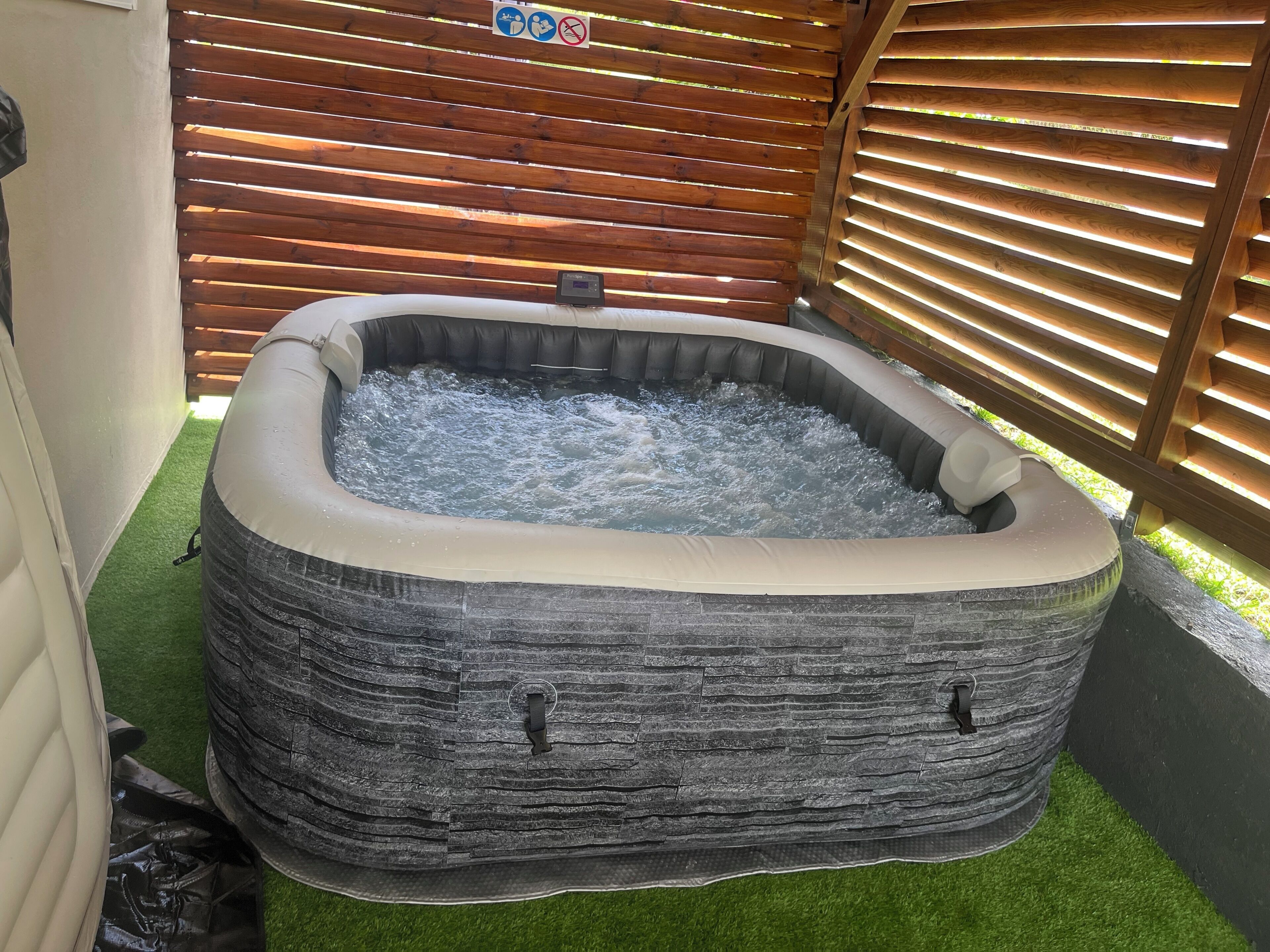 A hot tub with a stone-like exterior, surrounded by a wooden fence and artificial grass.