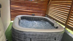 A hot tub with a stone-like exterior, surrounded by a wooden fence and artificial grass. - Aurore des îles-F3- 2bedroom with jacuzzi and terrace (Le François)