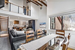 Un vaste espace de vie comprenant une table à manger en verre, des chaises en bois, un canapé et, au fond, une cuisine.