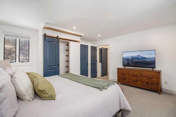 Une chambre à coucher comprenant un lit, un téléviseur, une commode et un placard avec des portes coulissantes.