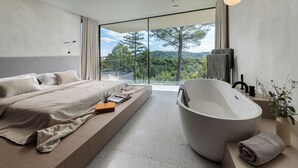 Ein modernes Schlafzimmer mit einem großen Bett, einer Badewanne und Blick ins Freie.