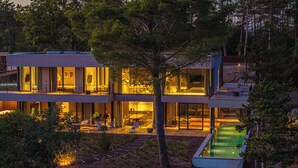 Ein modernes, zweistöckiges Haus mit Glasfassade, Sitzgelegenheiten im Freien und einem Swimmingpool.