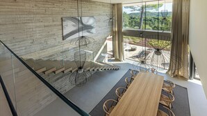 Ein modernes Interieur mit einem Holzesstisch, Stühlen, einer Treppe und einem großen Fenster mit Blick auf Grünflächen.