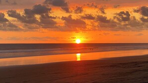A sunset over a beach with the sun visible near the horizon. - Vrbo Property (Parrita)