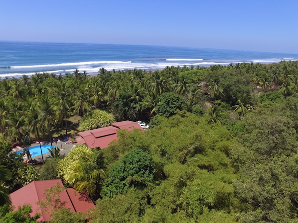 Ein Küsteneigentum mit Swimmingpool, Gebäuden mit roten Dächern, üppiger tropischer Vegetation und Blick aufs Meer.