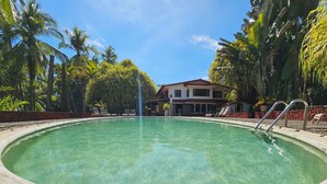 A clear pool with a circular shape, surrounded by lounge chairs and palm trees. - Vrbo Property (Parrita)