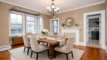 A dining room with a wooden table, six chairs, a chandelier, a fireplace, and large windows.