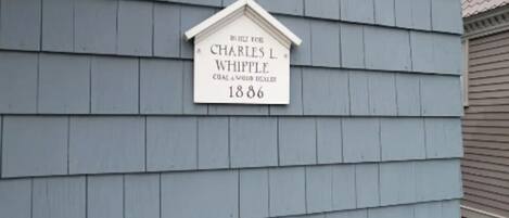 Un cartel con el nombre 'Charles L Whipple' y el año '1886' en una casa con tejas grises.