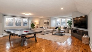 A living room with a ping pong table, a sofa, a coffee table, and a TV.