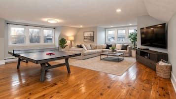 A living room with a ping pong table, a sofa, a coffee table, and a TV.