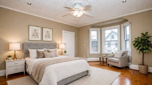 A bedroom with a bed, bedside tables, a chair, a plant, and a window.