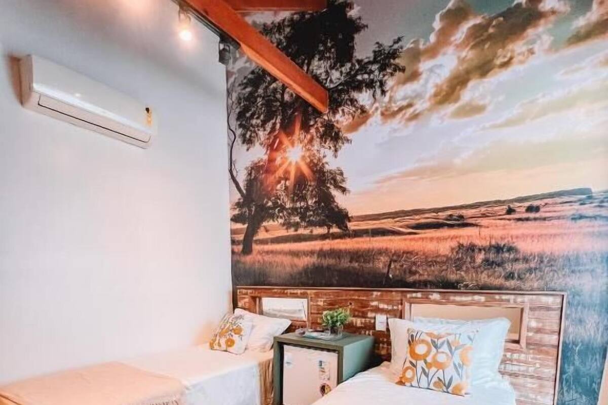 A room with two beds, a nightstand, and a wall mural of a sunset landscape.