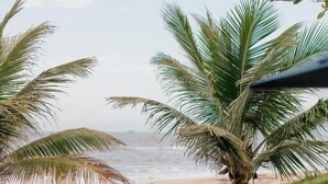 A patio with a chair and table, a thatched structure, and a view of the beach. - Casa cancun hotel boutique e eventos (Penha)