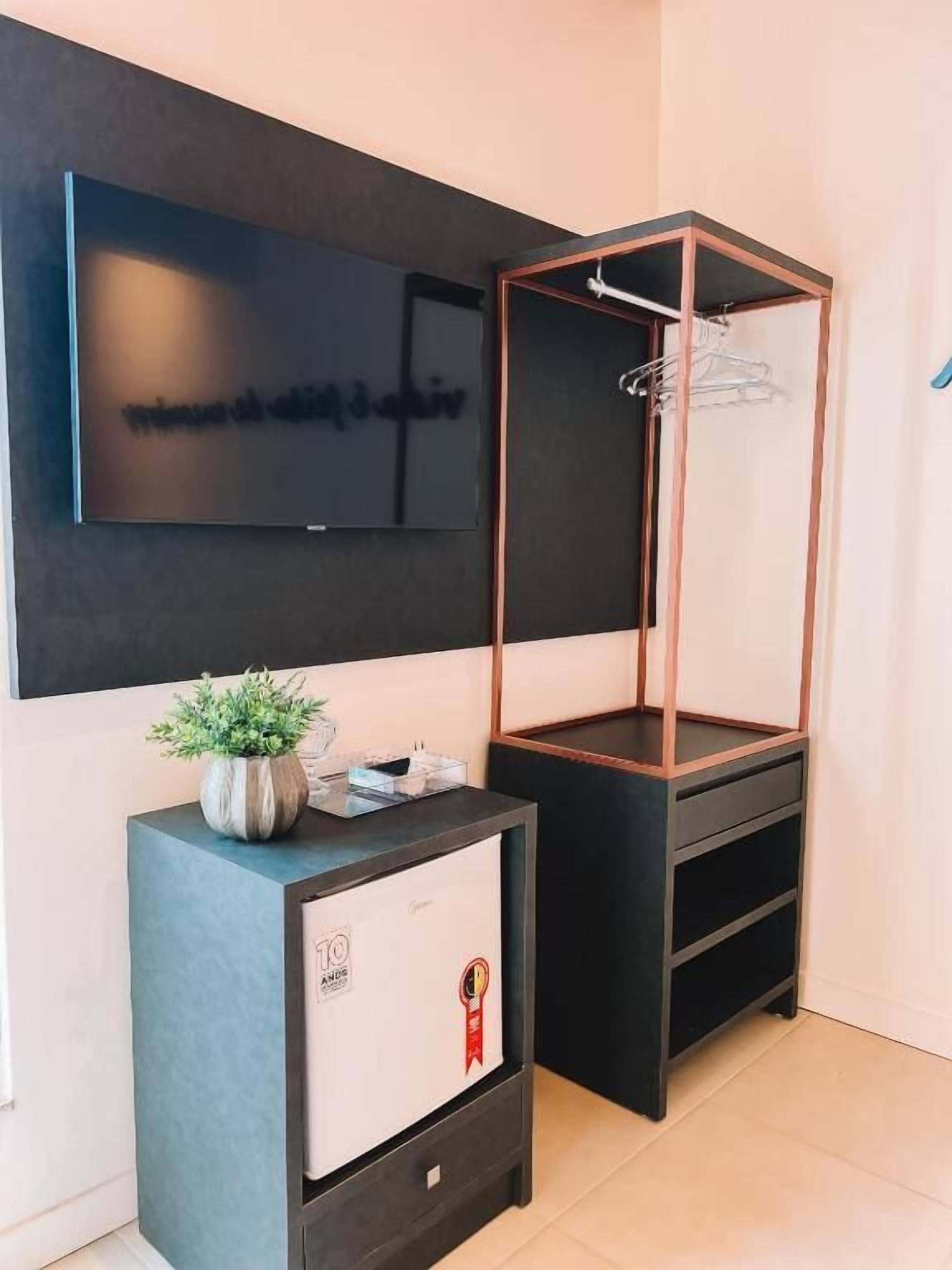 Une chambre moderne avec un téléviseur fixé au mur, un meuble noir orné d’une plante et une armoire en bois avec un miroir.