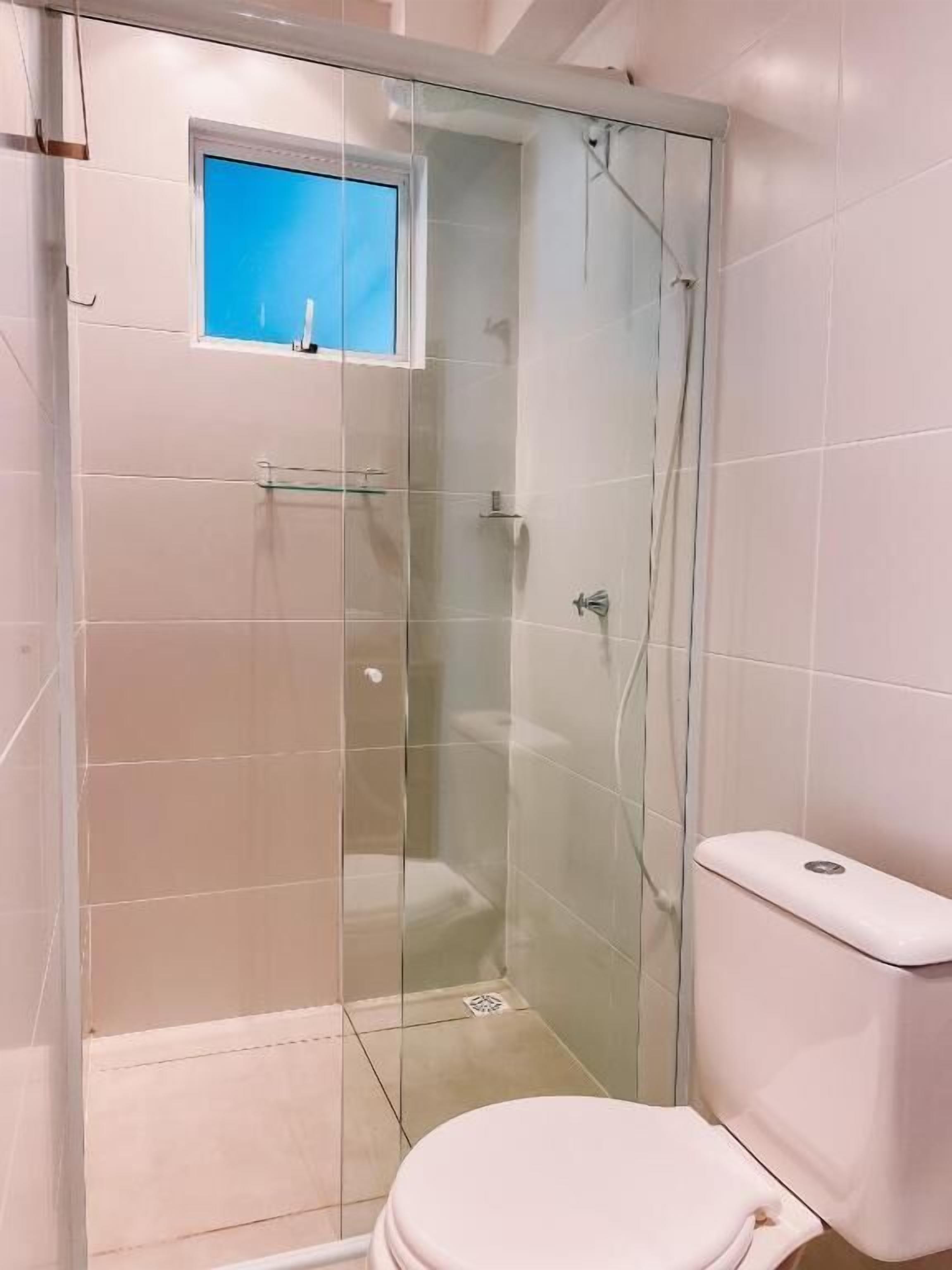 A bathroom with a glass-enclosed shower, a toilet, and a small window.