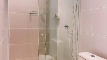 A bathroom with a glass-enclosed shower, a toilet, and a small window.