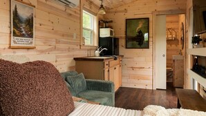 En stuga med träpanel på insidan, ett litet kök, en soffa och en målning som föreställer ett berglandskap.