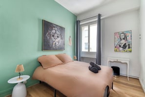 Une chambre à coucher avec un lit, une table de chevet, une lampe, un radiateur et des œuvres d’art accrochées aux murs.