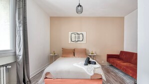 Un dormitorio con una cama, un sofá rojo, una lámpara colgante y una obra de arte enmarcada en la pared.