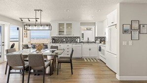 A modern kitchen with white cabinets, a dining area with a glass table, and a view of the ocean. - Promenade 403 - Oceanfront Oasis - Magical Views (Seaside)