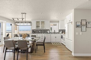 A modern kitchen with white cabinets, a dining area with a glass table, and a view of the ocean.