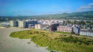 A coastal town with modern buildings, a beach, and green hills in the background. - Promenade 403 - Oceanfront Oasis - Magical Views (Seaside)