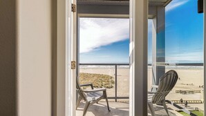A balcony with two chairs, a view of the beach, and a clear sky. - Promenade 403 - Oceanfront Oasis - Magical Views (Seaside)