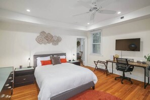 A bedroom with a bed, desk, chair, TV, and ceiling fan.